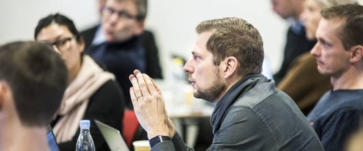 Mand sidder i klasselokale, og er i gang med at sige noget i plenum. Rundt om sidder andre, og lytter på manden.